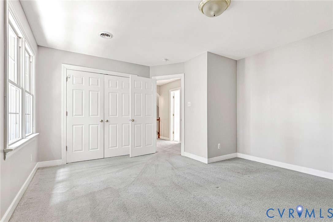 Light gray carpeting, white trim, white six-panel bi-fold closet doors, and a window with white sills and framing