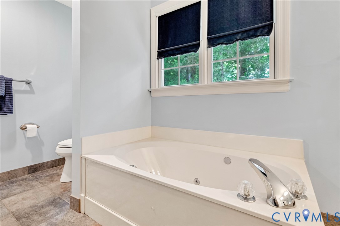 Built-in jetted tub with chrome fixtures, tiled flooring, and a window with white trim