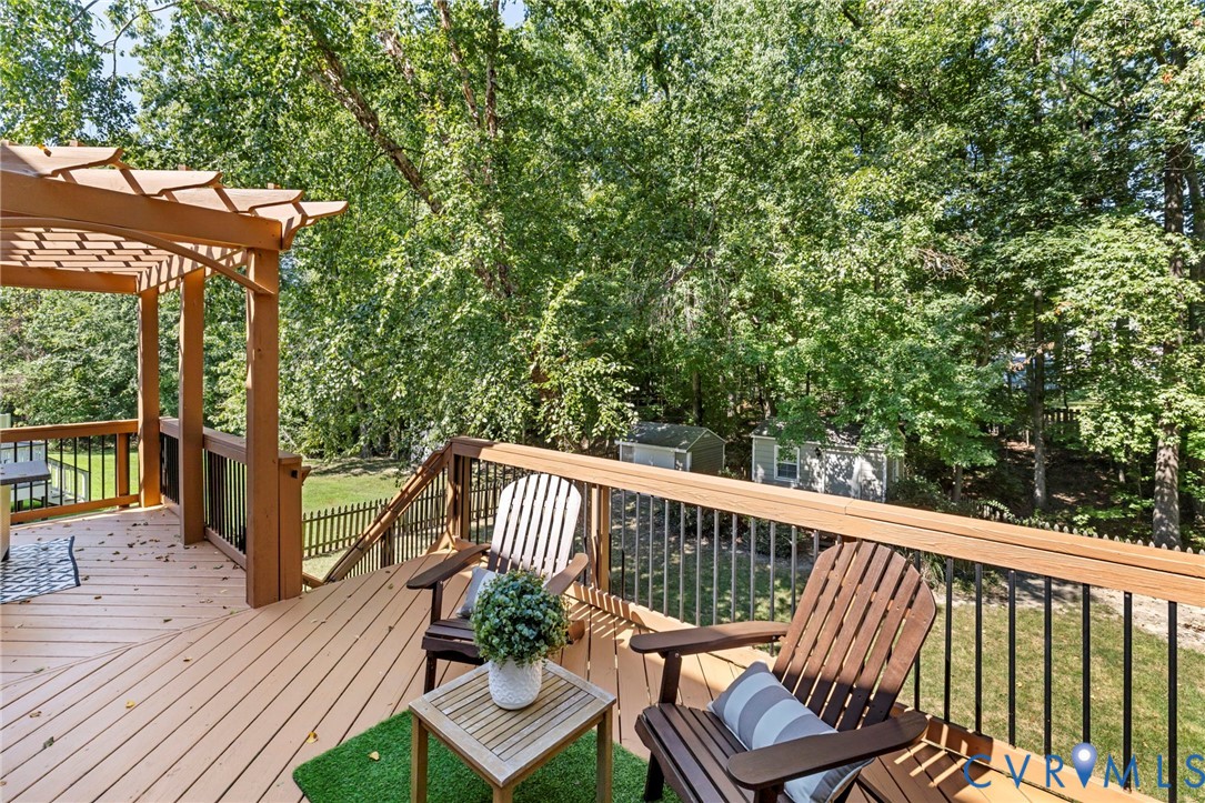 Expansive outdoor deck with a pergola, wood railing with black balusters, and a backyard with mature trees