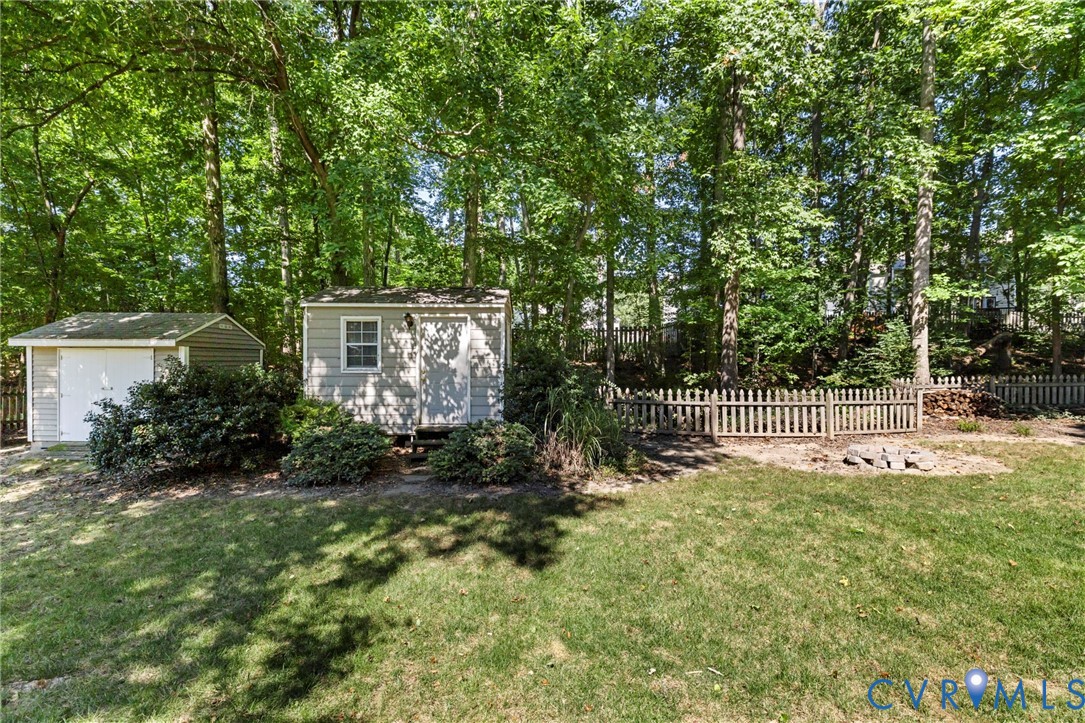 Expansive backyard featuring two exterior storage sheds, mature trees, and a wooden picket fence