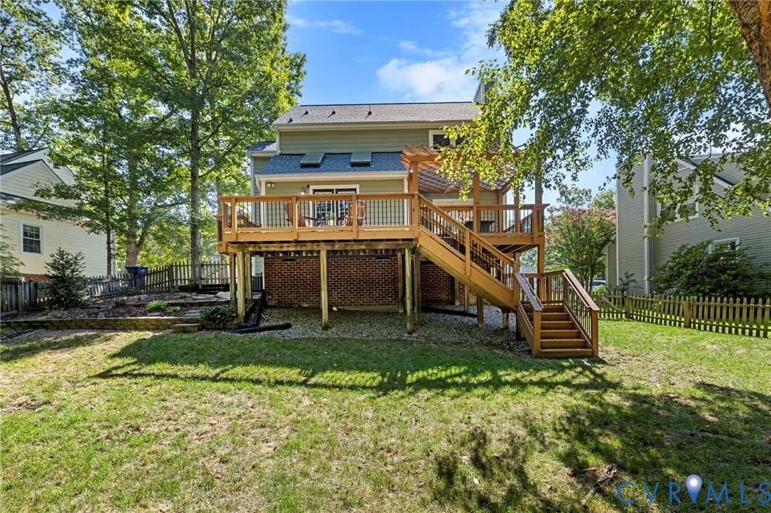 Multi-level wood deck with stairs leading to a spacious lawn, featuring a brick foundation and partial privacy fencing