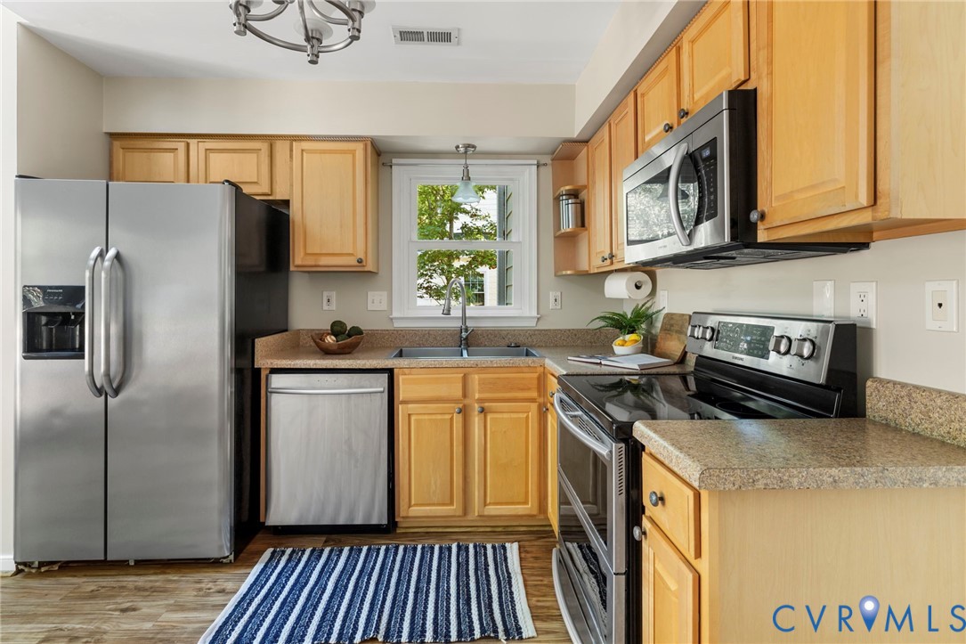 Kitchen featuring wood-finish cabinetry, stainless steel appliances, speckled countertops, and wood-finish flooring