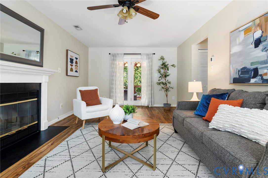 Living space featuring wood-finish flooring, a fireplace with a white mantel, and double doors opening to an exterior area Living space featuring wood-finish flooring, a fireplace with a white mantel, and double doors opening to an exterior area
