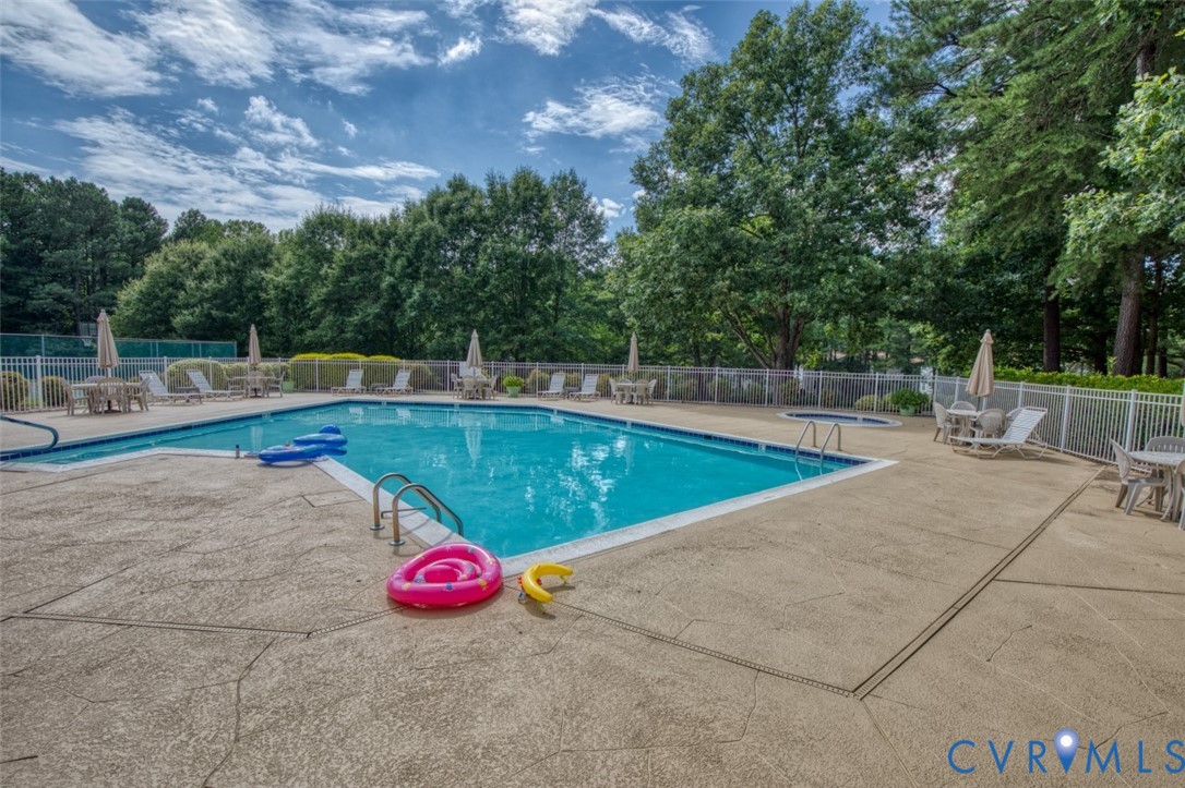 Resort-style in-ground swimming pool with crystal-clear water, surrounded by expansive concrete decking and white vinyl fencing