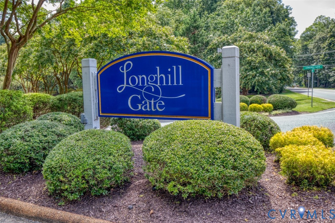 Longhill Gate Community Entrance featuring an elegant blue and silver monument sign with refined landscaping, including manicured boxwood hedges and mature shade trees framing the gated community access