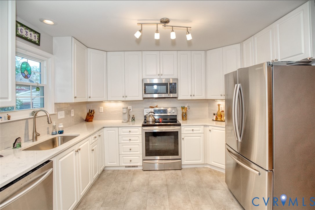 White cabinetry, stainless steel appliances, light-toned countertops, and a tiled backsplash