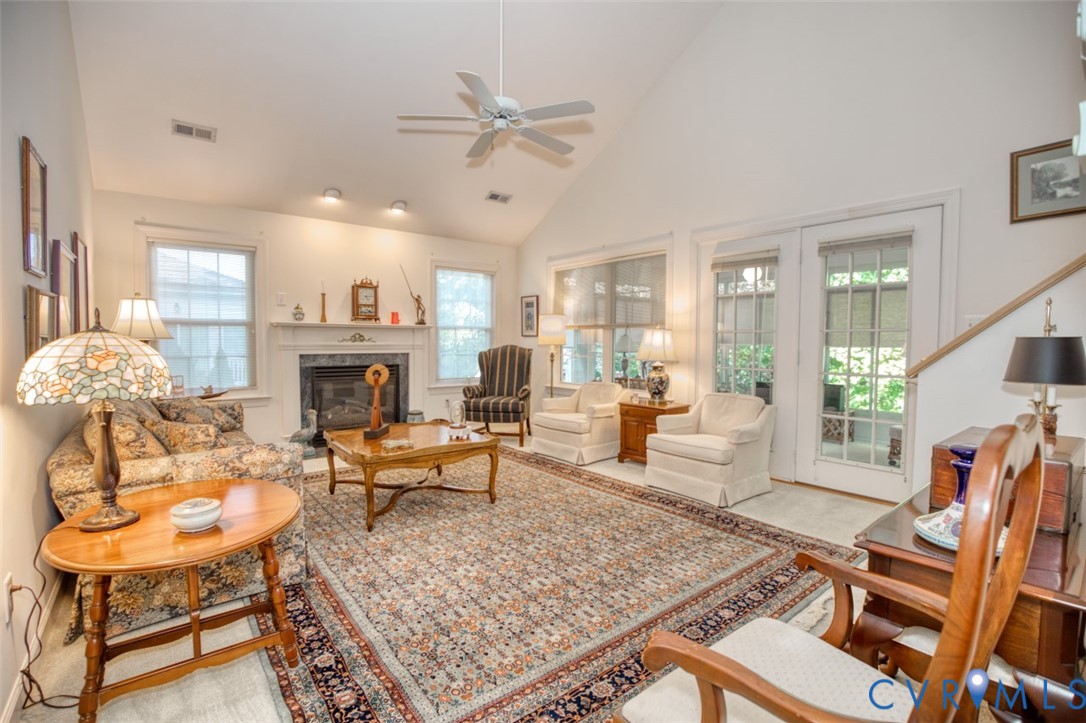 Vaulted ceiling with a ceiling fan, fireplace with a mantel, multiple windows, and exterior access via double glass-paneled doors