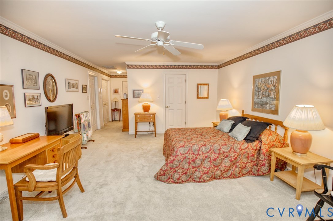 Spacious primary bedroom with soft carpet flooring, ceiling fan with integrated lighting, and abundant natural light from multiple windows