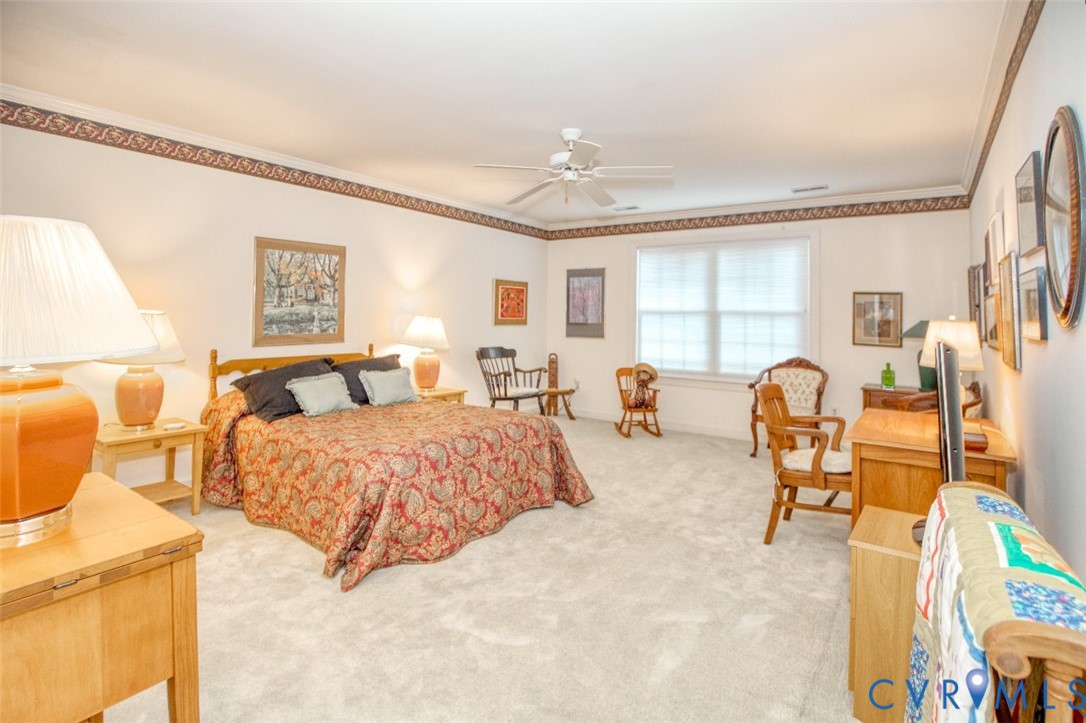 Spacious primary bedroom suite offering abundant natural light from multiple windows, wood-finish flooring throughout, decorative ceiling detail with crown molding, and ample room for bedroom furnishings and separate seating areas