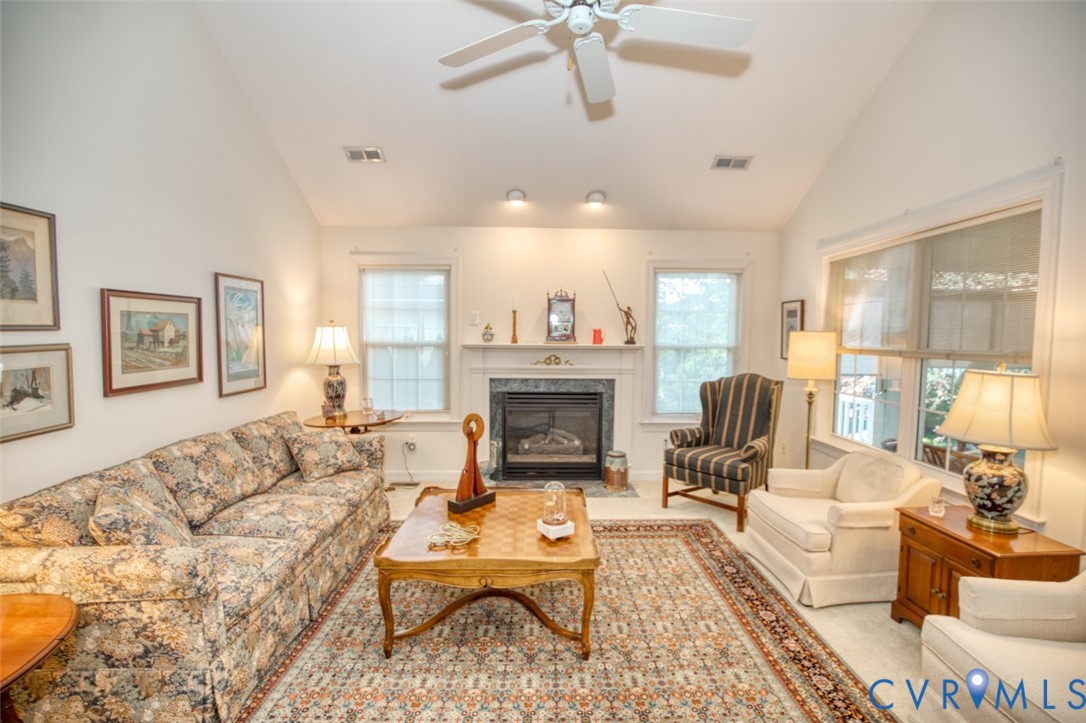 Bright, light-filled living room featuring vaulted ceilings with ceiling fan, gas fireplace with surround, recessed lighting, and French doors with transom windows opening to natural light