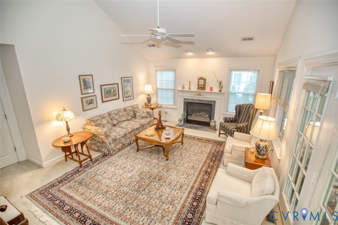 Vaulted ceiling with a ceiling fan, fireplace with a mantel, recessed lighting, and multiple windows