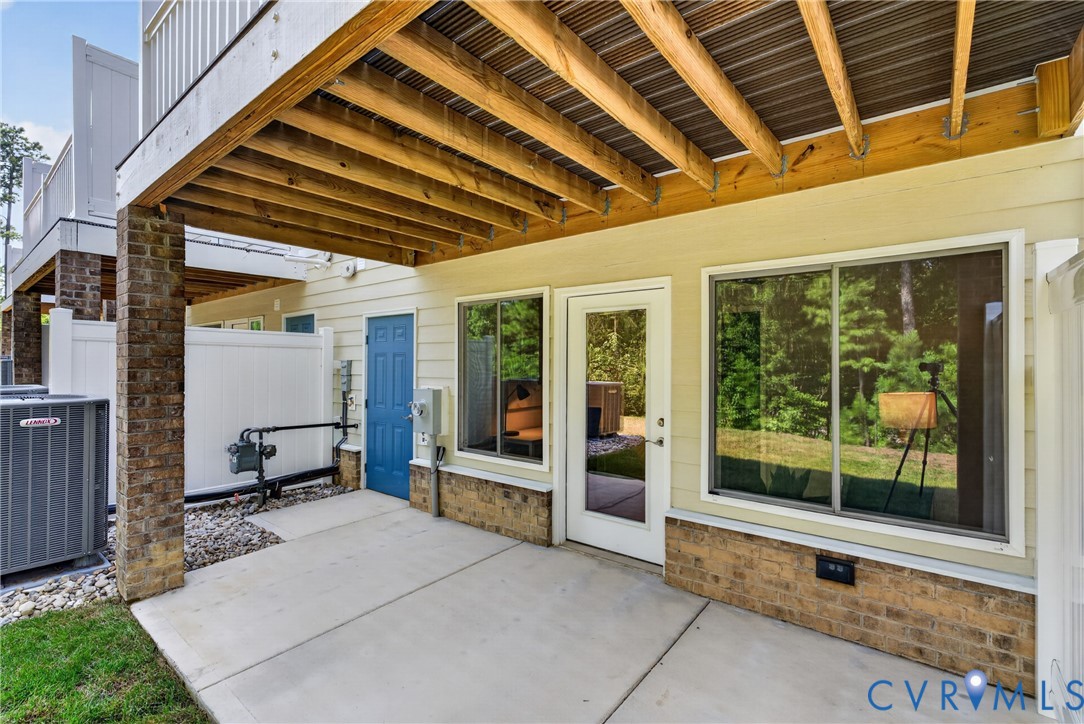 Concrete patio with brick columns, private white fencing, an exterior door, and a large sliding window