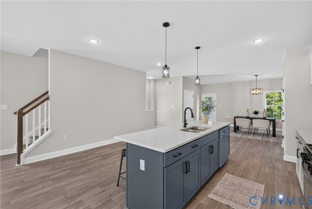 Kitchen island with a white countertop and dark cabinetry, stainless steel sink with a matte black faucet, wood-finish flooring, and recessed ceiling lighting