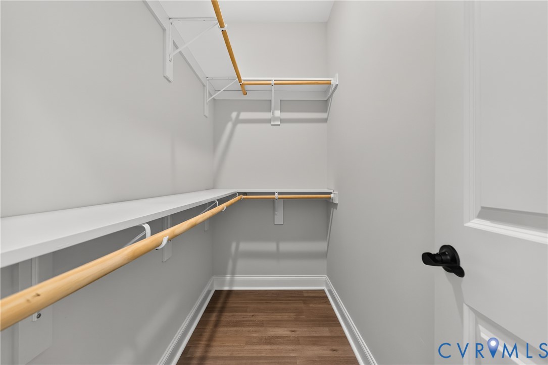 Walk-in closet featuring white shelving, wood-finish flooring, and a panel door with black hardware