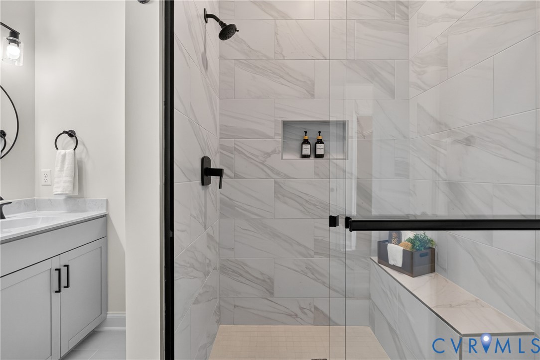 Walk-in shower with large format wall tiling, built-in shelving, and a shower bench