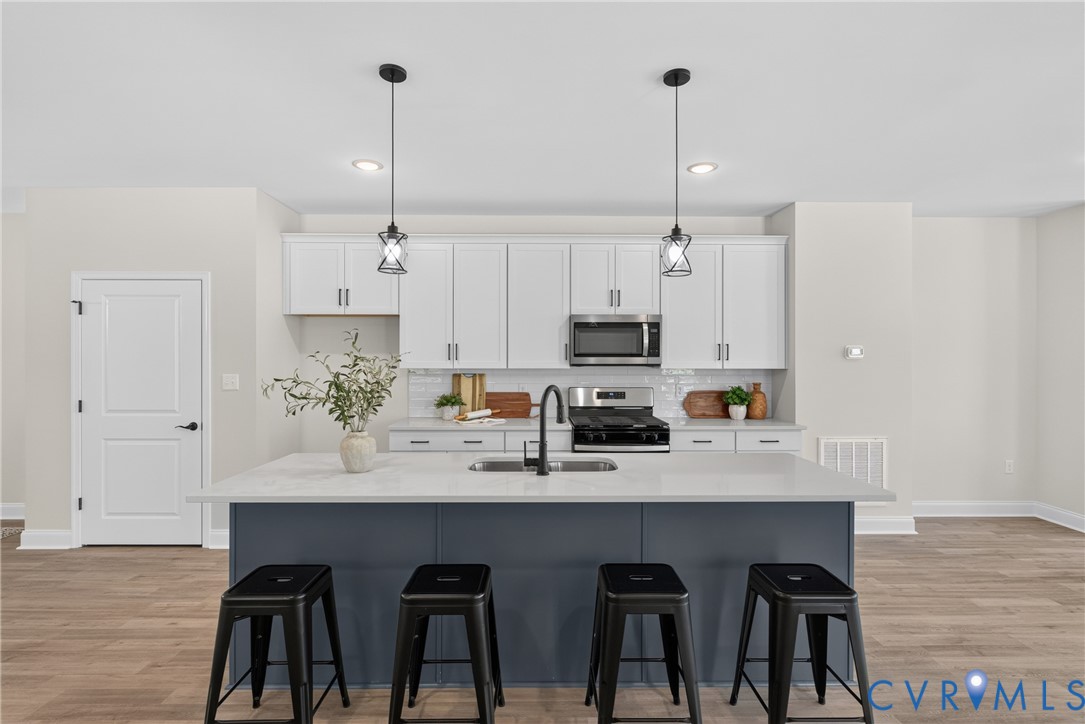 Kitchen featuring a large island with seating, pendant lighting, stainless steel appliances, white cabinetry, and wood-finish flooring