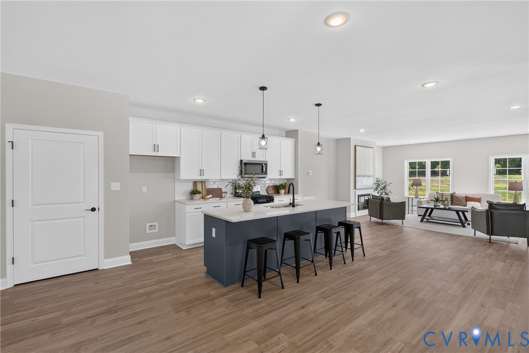 Kitchen featuring white cabinetry, a dark-toned island with seating, a white backsplash, and wood-finish flooring