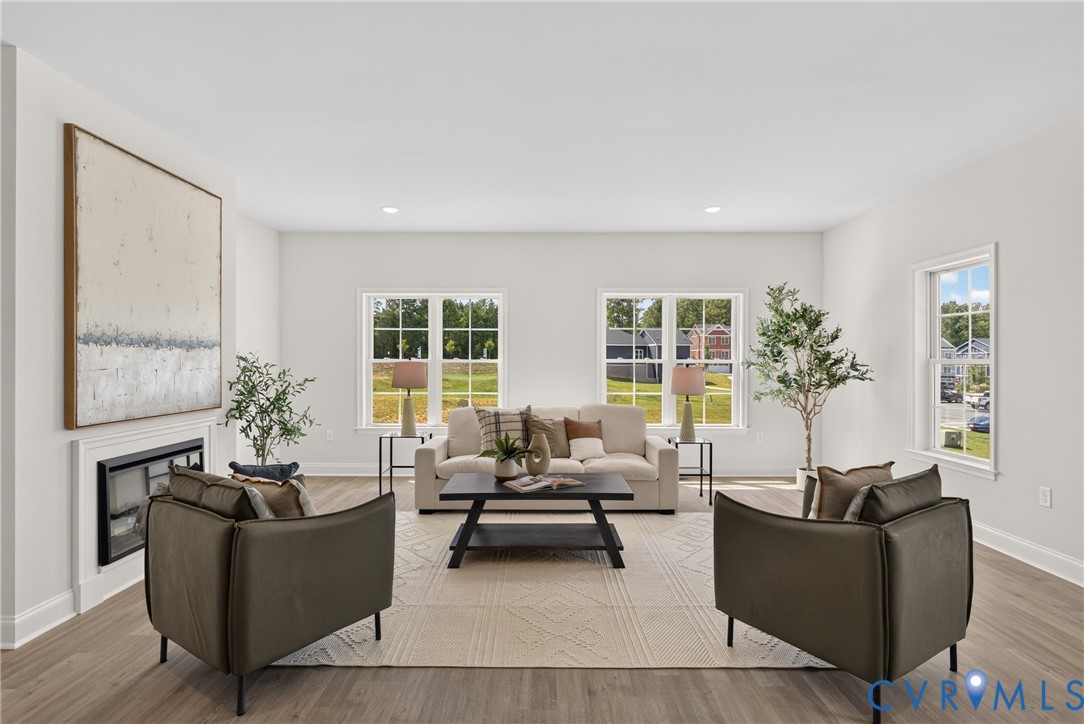 Bright open-concept living space with recessed lighting, wood-finish flooring, and a fireplace with a white mantel