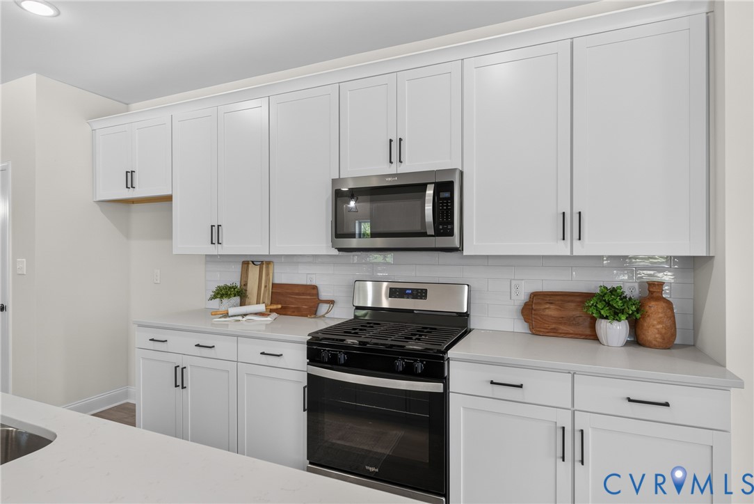 White shaker-style cabinetry with matte black hardware, stainless steel microwave, gas range with oven, light-toned countertop, and white subway tile backsplash