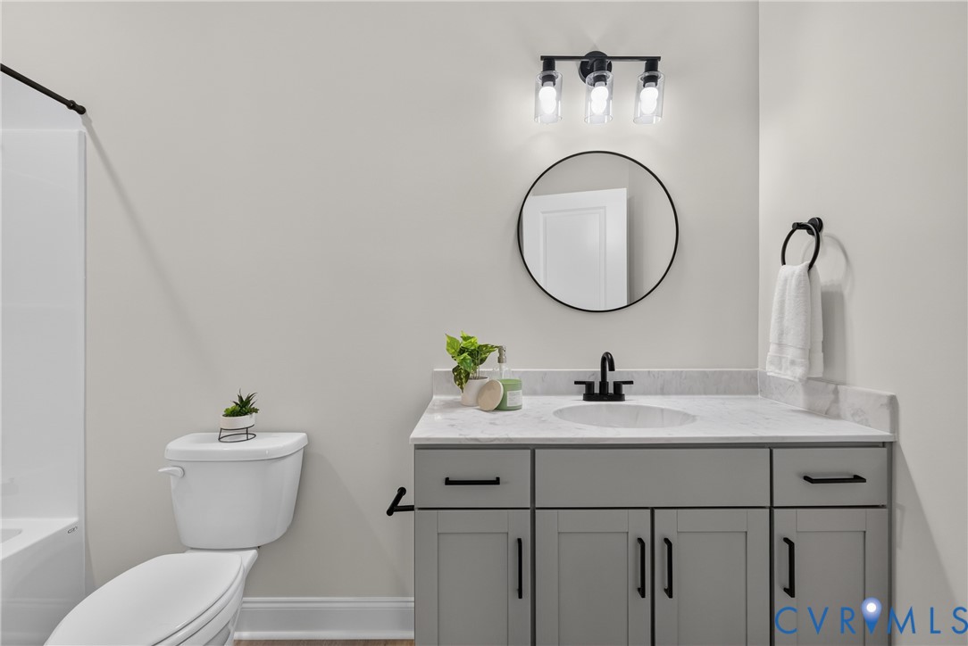 Vanity with a light gray finish and matte black hardware, white countertop, round mirror, and a three-light fixture