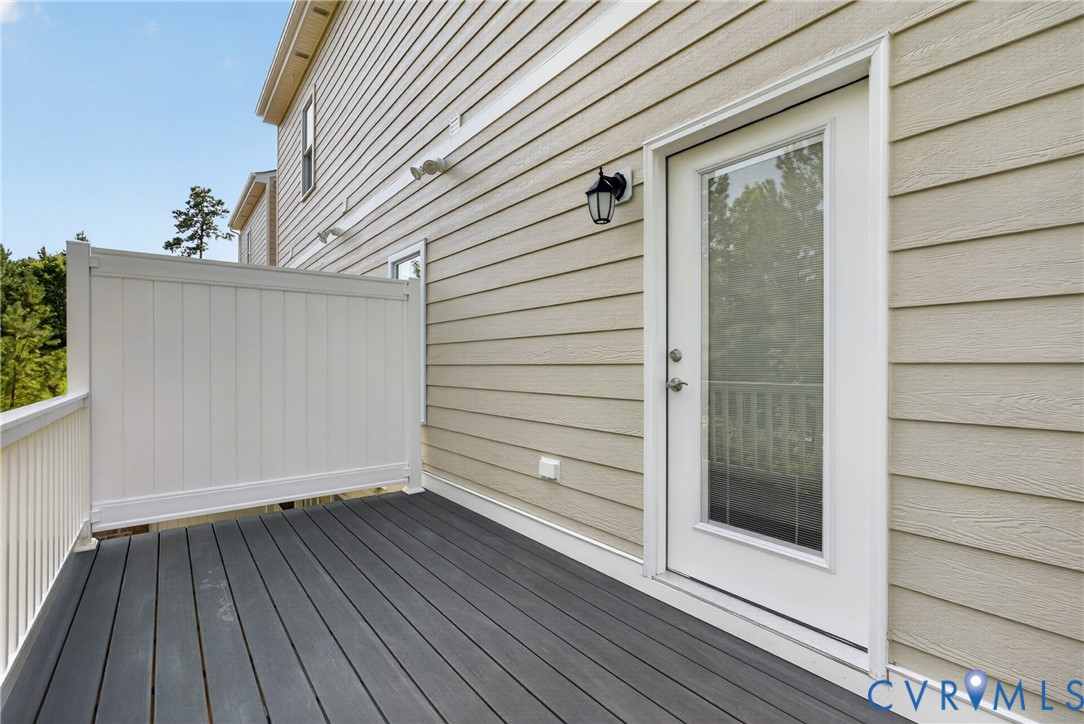 Exterior deck featuring composite decking, white vinyl railing, and a full-light door with a matte black lantern-style sconce