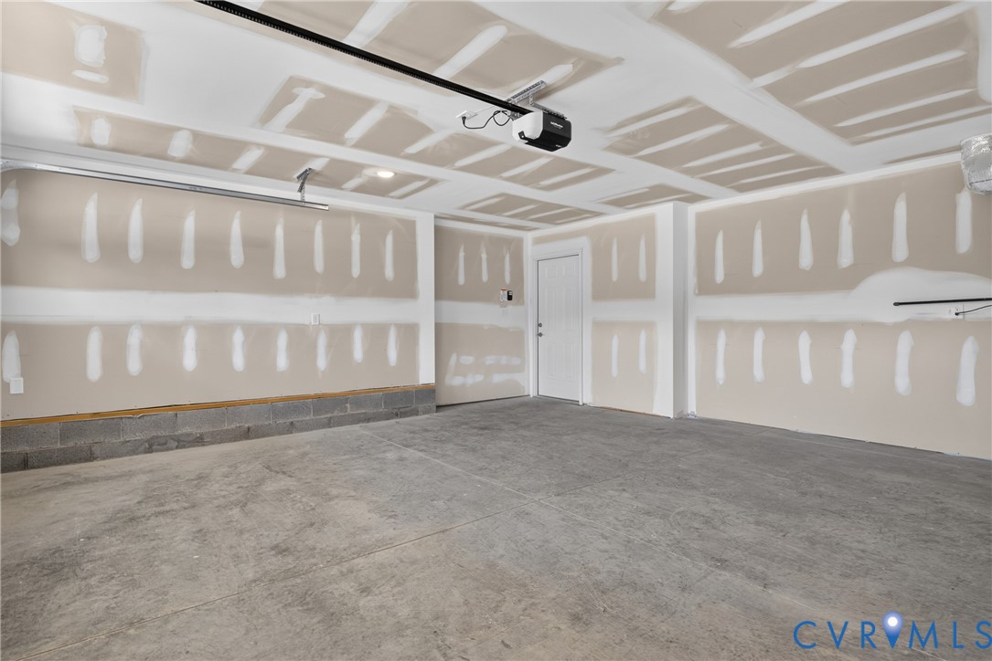 Concrete flooring, drywall-ready walls, white panel door, exposed ceiling joists, garage door mechanism