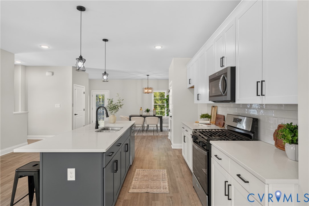 Kitchen featuring a central island with a sink, white countertops, white upper and lower cabinetry, stainless steel appliances, and wood-finish flooring