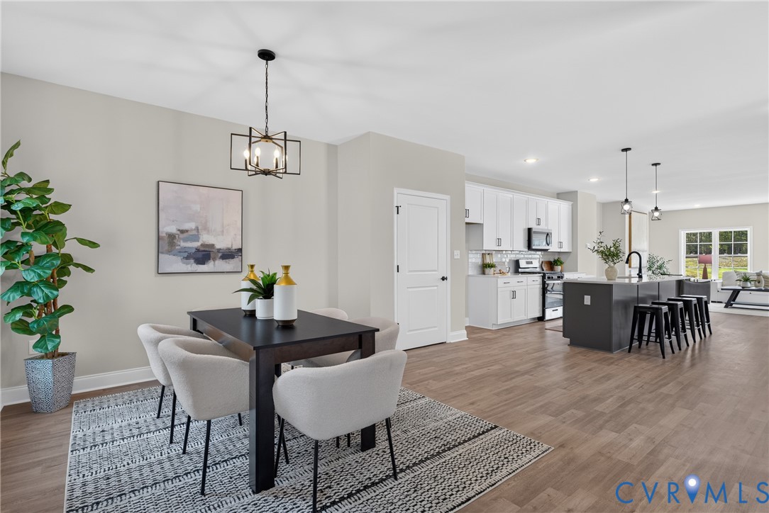 Expansive wood-finish flooring throughout, modern kitchen island with seating, white shaker cabinetry, stainless steel appliances, and a contemporary dining room chandelier