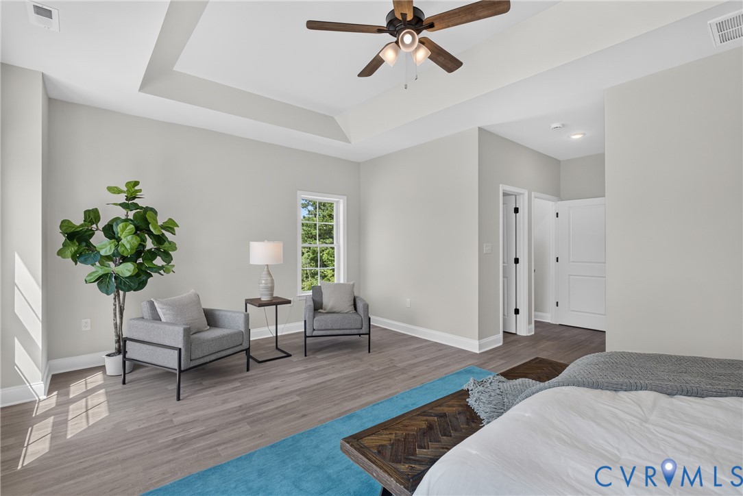 Tray ceiling with a ceiling fan, wood-finish flooring, white trim, and a window