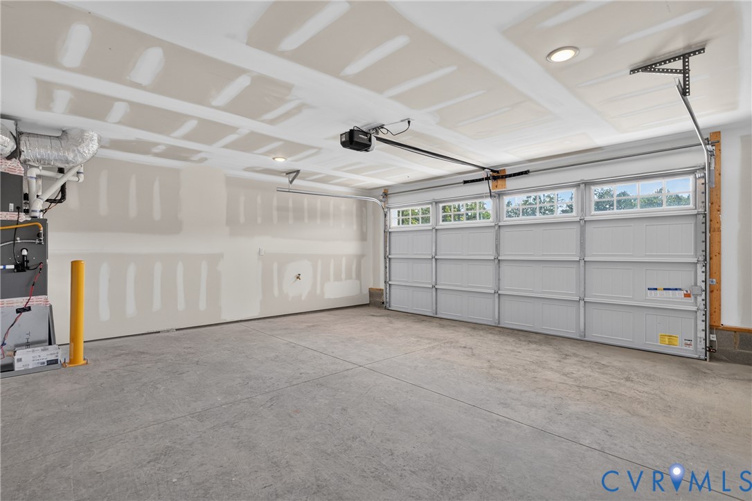 Spacious garage with a concrete floor, equipped with a paneled garage door featuring transom windows and an automatic opener