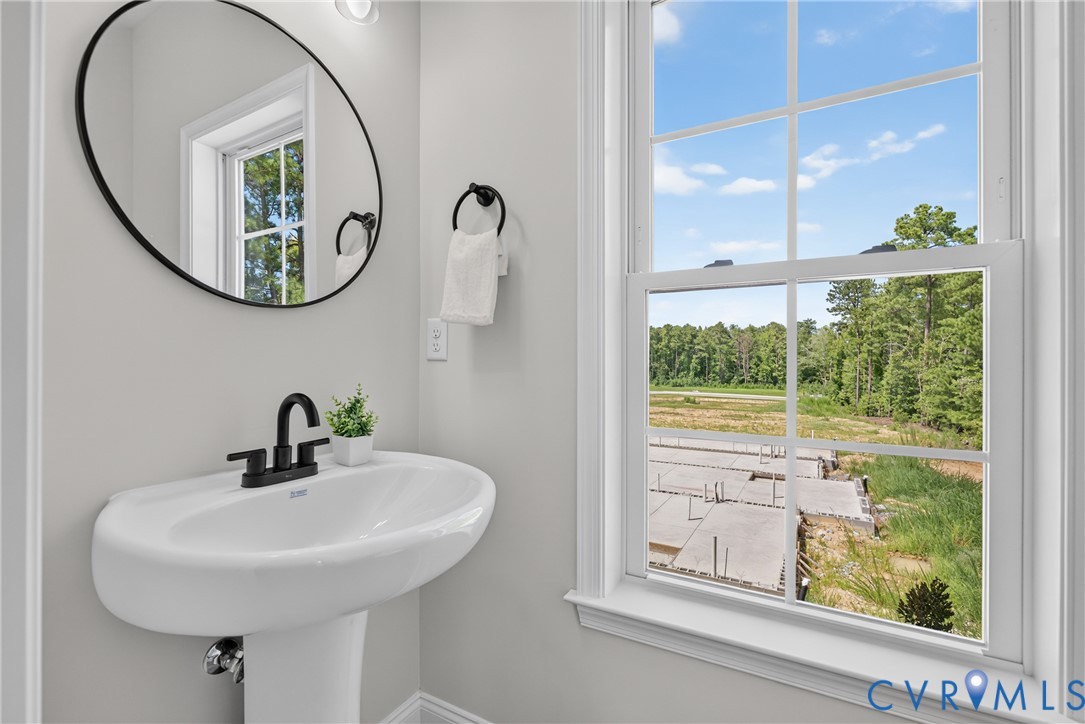 Pedestal sink with matte black faucet, framed mirror, and natural light from a large window