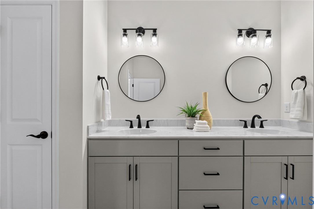 Double vanity with light gray cabinetry, white countertops, dual integrated sinks, and individual round mirrors