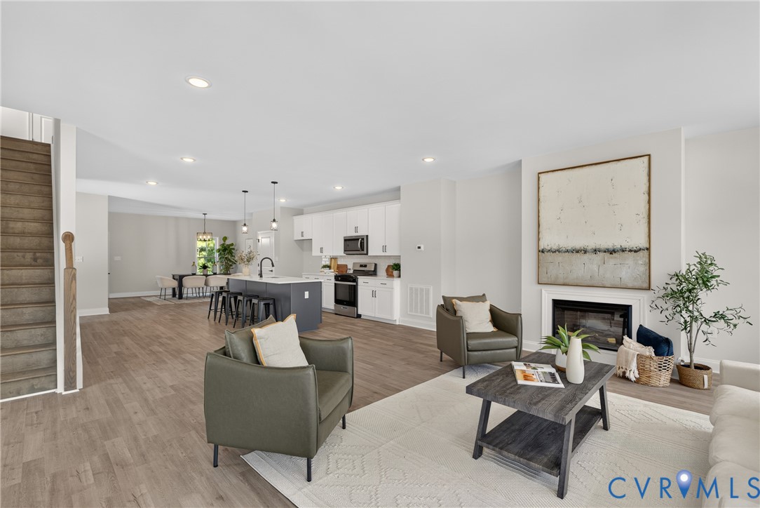 Spacious open-concept living area featuring wood-finish flooring, a contemporary fireplace, recessed lighting, and a kitchen island with pendant lighting