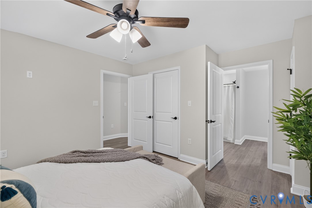 Ceiling fan with wood-finish blades, light gray walls, wood-finish flooring, white paneled doors, and matte black hardware