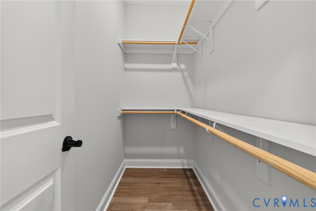 Walk-in closet with multiple white storage shelves, wood-finish hanging rods, and wood-finish flooring