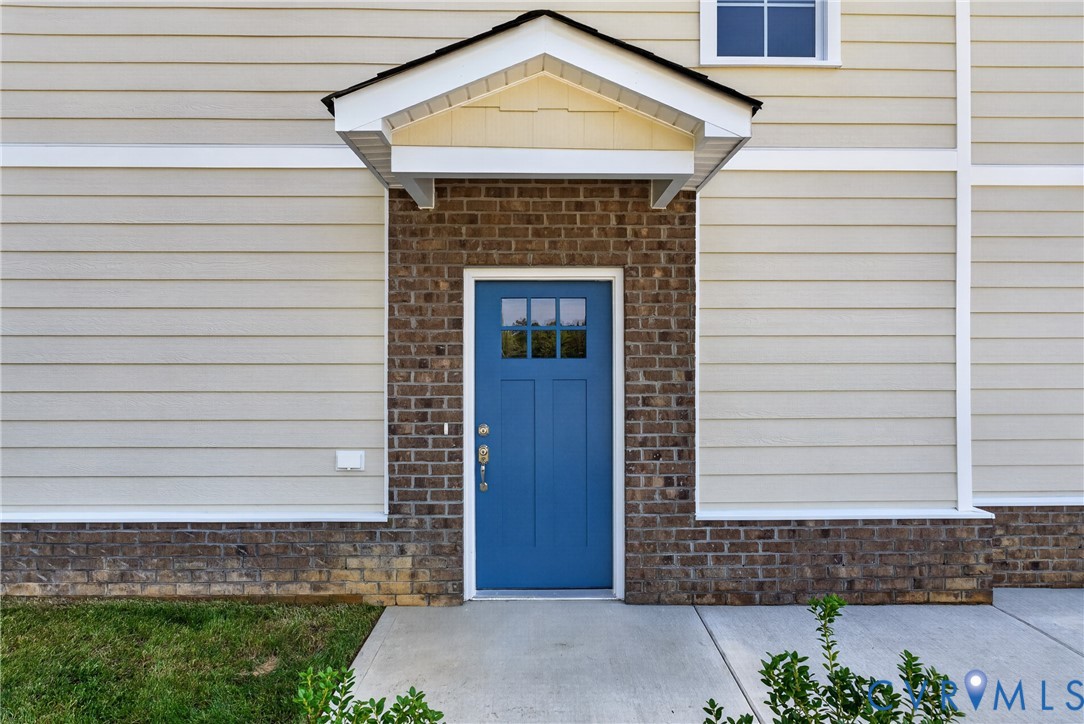 Entryway featuring a bright blue door with window panes, brick facade, and a covered porch overhang