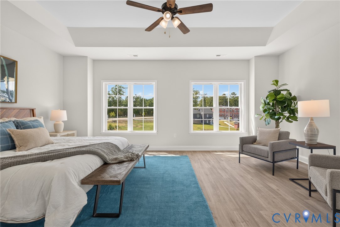 Tray ceiling with a ceiling fan, two double-hung windows, and wood-finish flooring