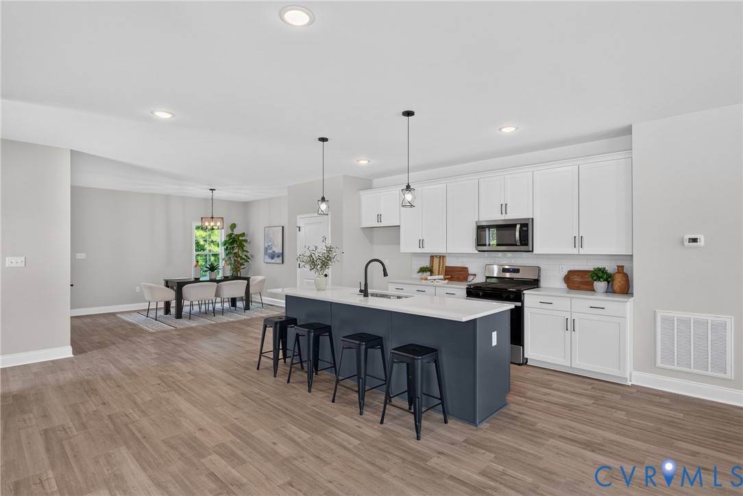 Open-concept kitchen featuring white cabinetry, a dark-toned island with seating, stainless steel appliances, and wood-finish flooring throughout