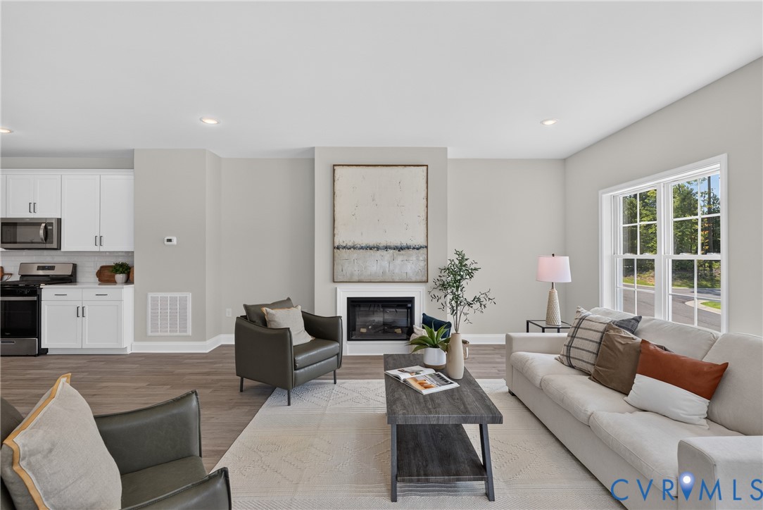 Open-concept living area featuring wood-finish flooring, recessed lighting, a built-in fireplace, and a large multi-pane window