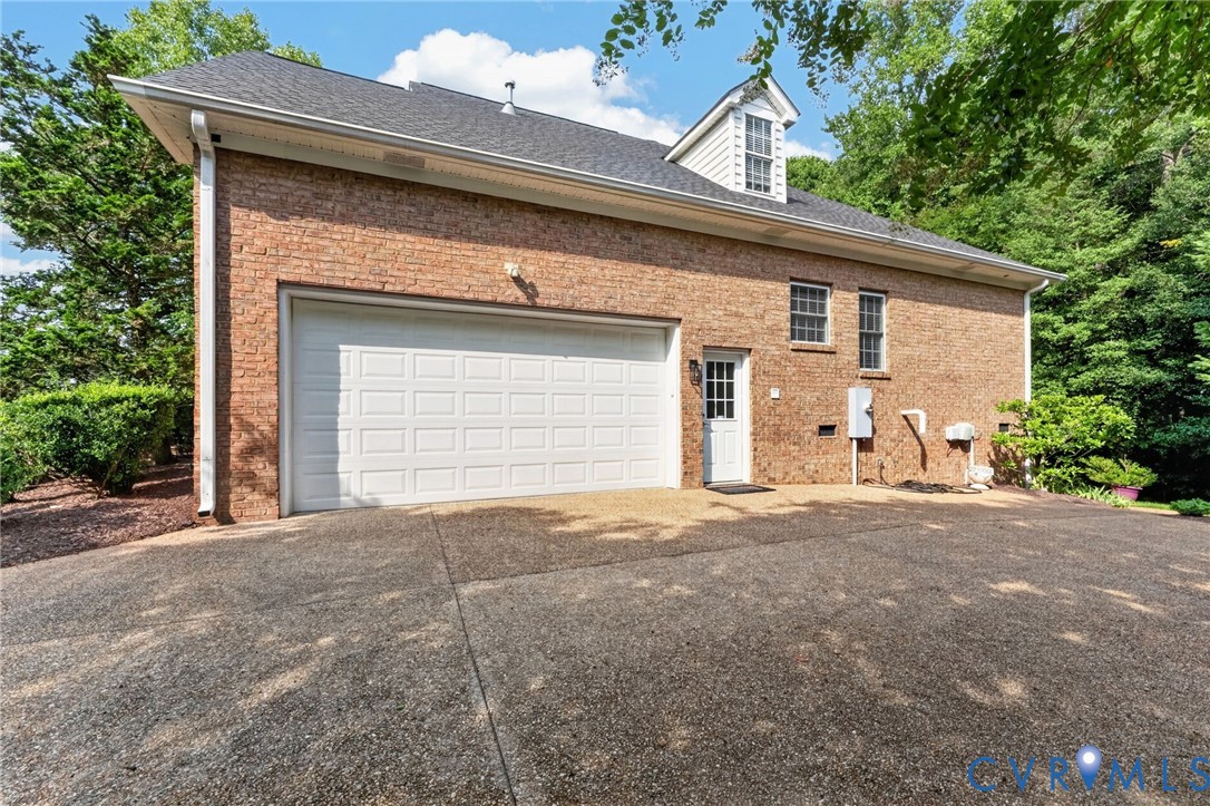 Brick Colonial home featuring a two-car garage with white paneled door, asphalt driveway, side-entry door with transom window, and multiple fenestration across the facade