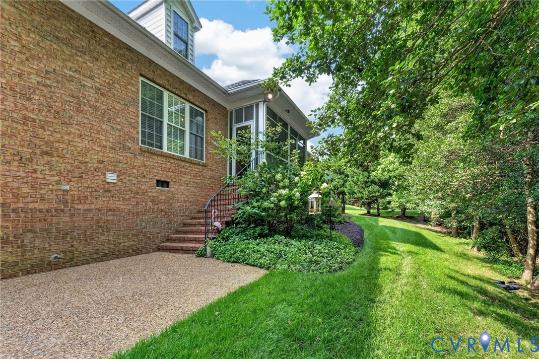 Brick exterior with a dormer, screened porch, stone paver patio, and expansive lawn with mature trees