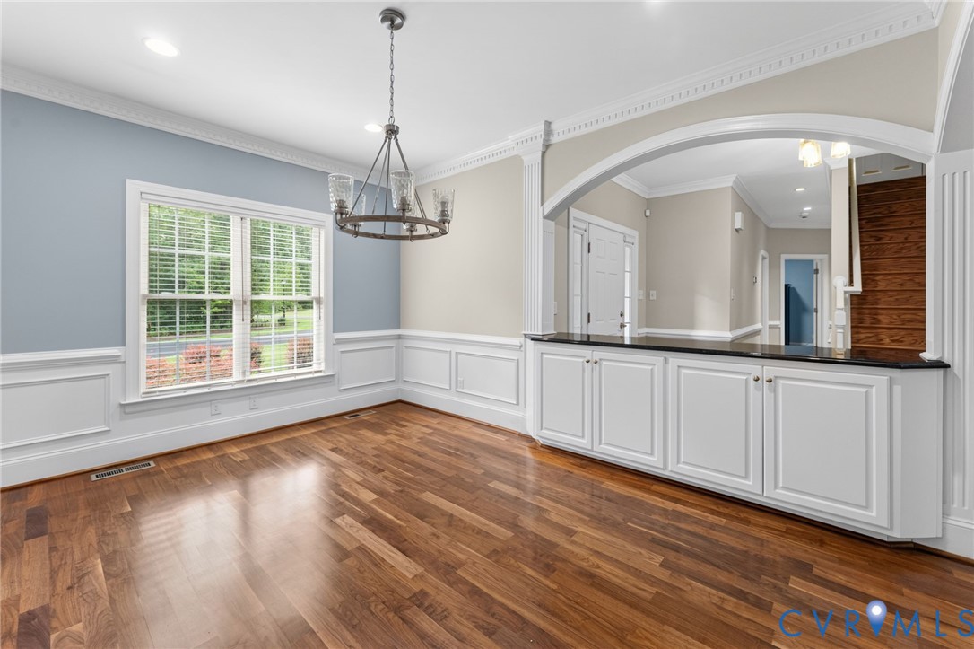 Wood-finish flooring, wainscoting, crown molding, built-in cabinetry with a dark countertop, and an arched entry