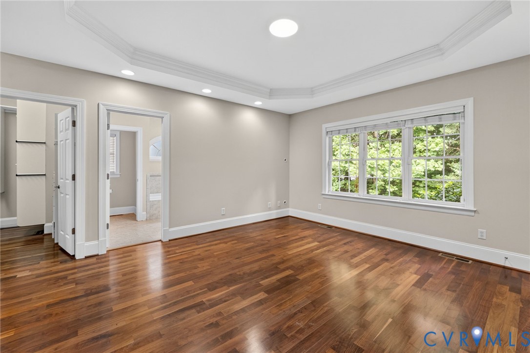 Bright, light-filled room showcasing rich wood-finish flooring, recessed ceiling lighting, and abundant natural light from triple-pane windows