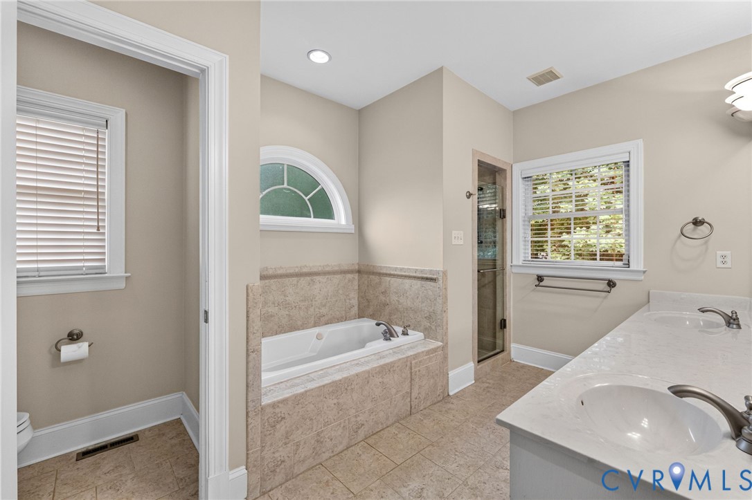 Spa-inspired primary bathroom featuring a soaking tub with tile surround, separate walk-in shower with glass enclosure, dual vanity with vessel sinks, tile flooring, recessed lighting, and a transom window providing natural light