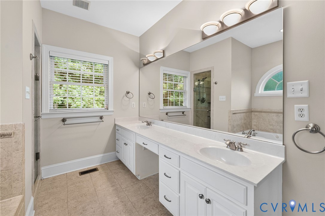 Spa-inspired primary bathroom featuring dual vanities with white cabinetry, an extended quartz countertop, and polished chrome fixtures