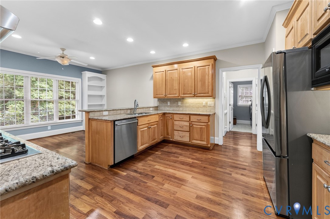 Spacious kitchen featuring warm wood cabinetry, stainless steel appliances, granite countertops, recessed ceiling lighting, and hardwood flooring throughout