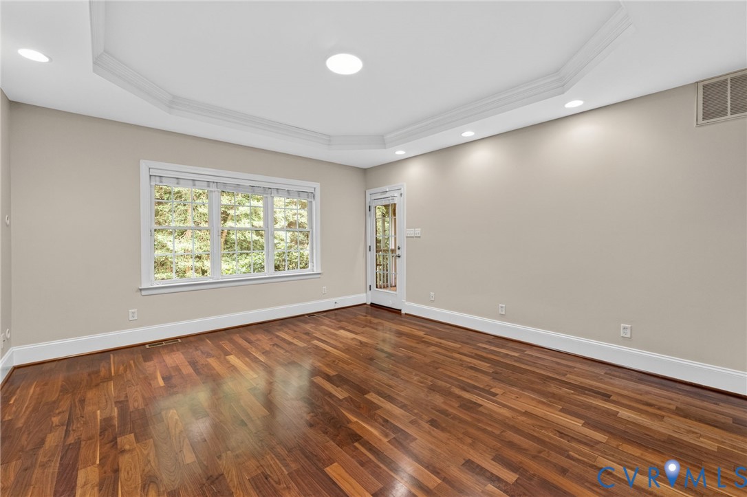 Spacious room featuring rich wood-finish flooring, recessed ceiling lighting, and abundant natural light from a triple-window configuration