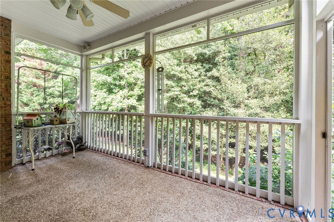 Screened porch with brick column, textured flooring, and a ceiling fan