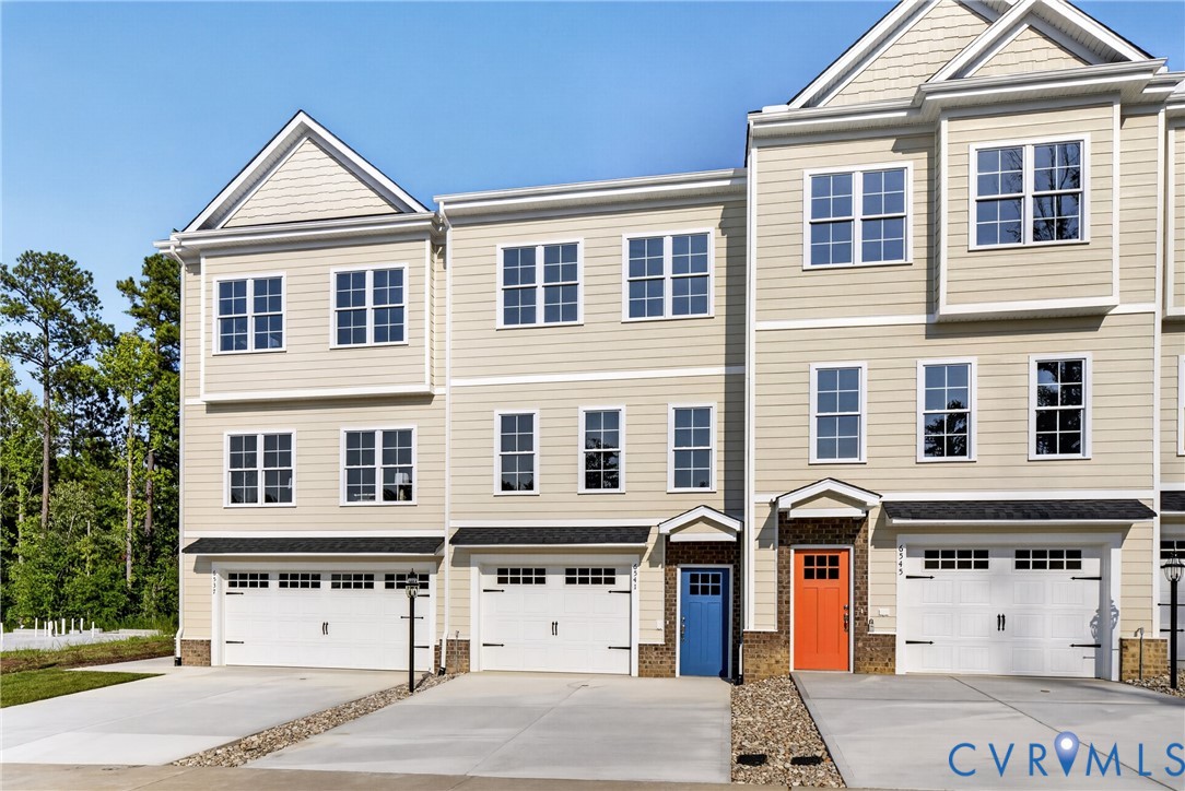 Three-story townhome with light-colored siding, multiple multi-pane windows, individual attached garages, and direct-entry front doors