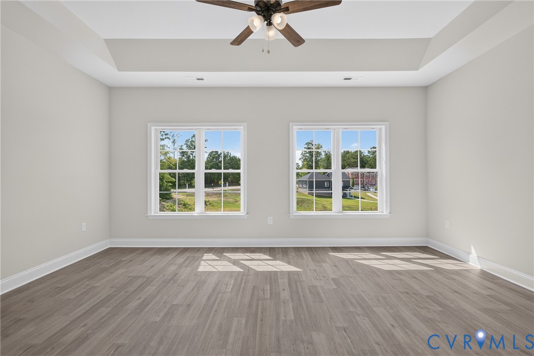 Tray ceiling, wood-finish flooring, ceiling fan, and two large windows